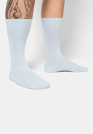 Light blue cotton socks with a ribbed cuff, featuring a smooth texture and a solid color design, shown on patterned tattooed legs.