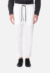 Pantaloni bianchi leggeri con vita elasticizzata e cordino nero, abbinati a sneakers nere con suole bianche.