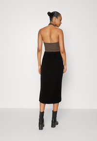 Svart midiskjørt med tett liv og sidesømmeposer, kombinert med en brun haltertop. Glatt stoff, minimalistsk design. Sorte ankelstøvler.
