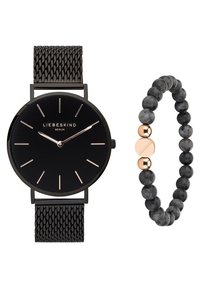 Zwarte polshorloge met mesh band, voorzien van een zwarte wijzerplaat en roségouden accenten; vergezeld van een kralenarmband in grijs en zwart met roségouden details.