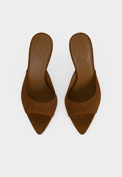 Paire de mules marron en daim à bout pointu, modèle slip-on avec côtés ouverts et nom de marque embossé à l’intérieur sur fond uni.