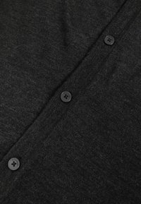 Cardigan noir en tissu doux et texturé. Il présente cinq boutons ronds noirs sur le devant, avec un motif côtelé subtil.