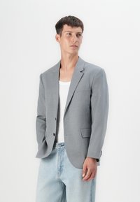 Gray blazer with notch lapels, single button closure, and two front pockets. Worn over a white tank top and blue denim jeans. Smooth texture.