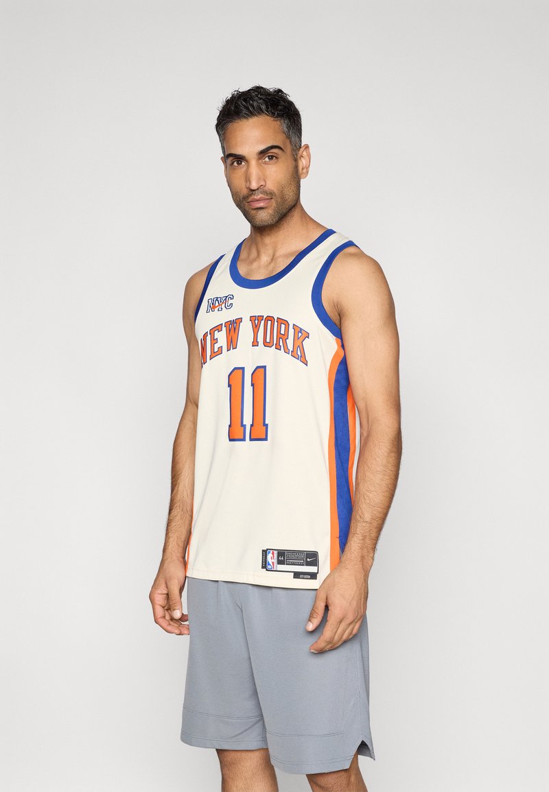 Basketball-Trikot in Creme, Blau und Orange mit dem Schriftzug "NEW YORK" und der Nummer 11 in fettem Druck. Getragen mit grauen Shorts, leichter Stoff.