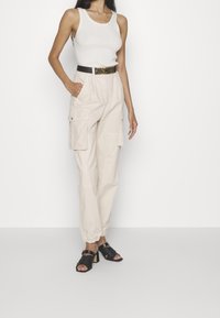 Beiga cargobyxor med flera fickor, kombinerade med en vit ribbad linne och svarta blockklacksandaler med texturerade remmar.