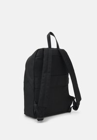 Mochila negra hecha de tejido texturizado, con correas anchas y un diseño estilizado que incluye un asa superior para un fácil transporte.