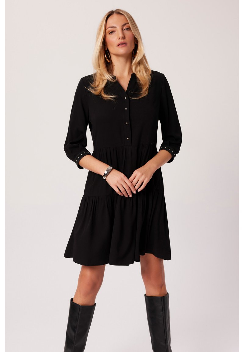 Czarna sukienka do kolan z przodem zapinanym na guziki oraz rękawami o długości trzech czwarci. Posiada marszczoną spódnicę i ćwiekowane detale na mankietach.