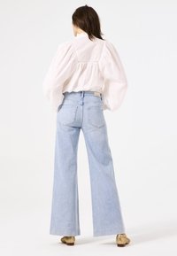 Jeans de pierna ancha de color azul claro, hechos de denim, con cinco bolsillos y una cinturilla entallada, combinados con una blusa blanca texturizada.