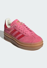 Sneaker em camurça rosa com pormenores em couro vermelho, três riscas brancas, língua texturizada e sola de borracha de goma. Detalhe de marcação em dourado presente.
