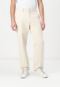 Lyse beige bukser laget av myk stoff med rett ben-design, med knappelukking og sidelommer, kombinert med hvite sneakers.