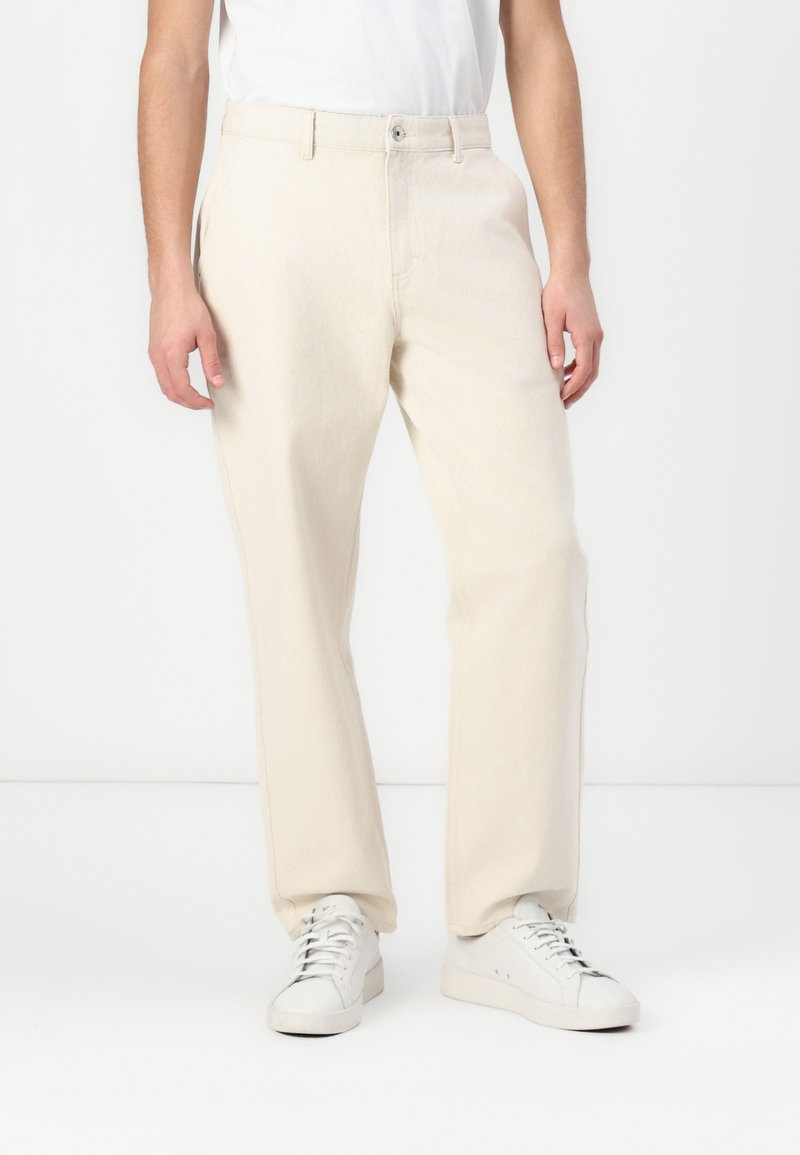 Lyse beige bukser laget av myk stoff med rett ben-design, med knappelukking og sidelommer, kombinert med hvite sneakers.