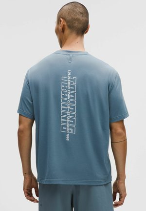 Hellblaues kurzärmeliges T-Shirt aus Baumwollmischung, mit vertikalem weißen Text auf der Rückseite: "LULULEMON TRAIN CLUB - GEGRÜNDET 1998."