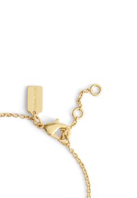 Guldkedjearmband med en hummerklämma, försedd med en rektangulär platt tagg graverad med "COACH." Slät textur och länkdesign.