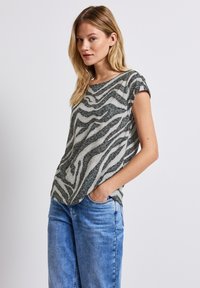 Top da donna a maniche corte verde chiaro con motivo a strisce zebrate, dotato di scollo rotondo e tessuto morbido e testurizzato. Abbinato a jeans azzurri.