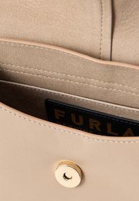 Beige színű bőr kézitáska sima felülettel, arany színű patentzárral, látható belső zsebekkel és márkacímkével.