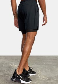 Black athletic shorts with an elastic waistband and side slits, layered over fitted black undershorts. Worn with black sneakers.