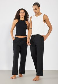 Débardeur noir en maille côtelée et pantalon noir ample avec cordon de serrage. L'homme porte un haut sans manches blanc. Les deux vêtements sont simples et doux.