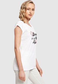 Hvid bomulds t-shirt med et trykt design med teksten "Kærlighed er i luften", accentueret med røde hjerter. Korte ærmer, afslappet pasform.