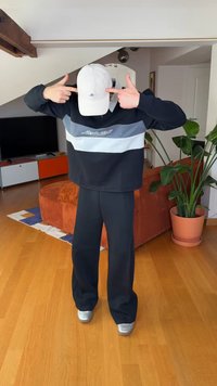 Svart och grå oversized sweatshirt med logotyp, matchande mörka byxor och en ljus keps, kombinerat med silvriga skor.