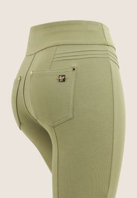 Leggins verdes elásticos con una cintura alta, que cuentan con dos bolsillos traseros, herrajes en tono dorado y detalles de costura horizontal.