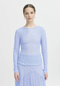 Top a maniche lunghe in pizzo azzurro chiaro con design aderente, delicato motivo floreale e scollatura rotonda, abbinato a una gonna in pizzo coordinata.