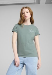 Zelené bavlnené tričko s krátkymi rukávmi, so vyšitým logom "Puma". Skombinované s svetlo modrými džínsami. Hladká textúra.