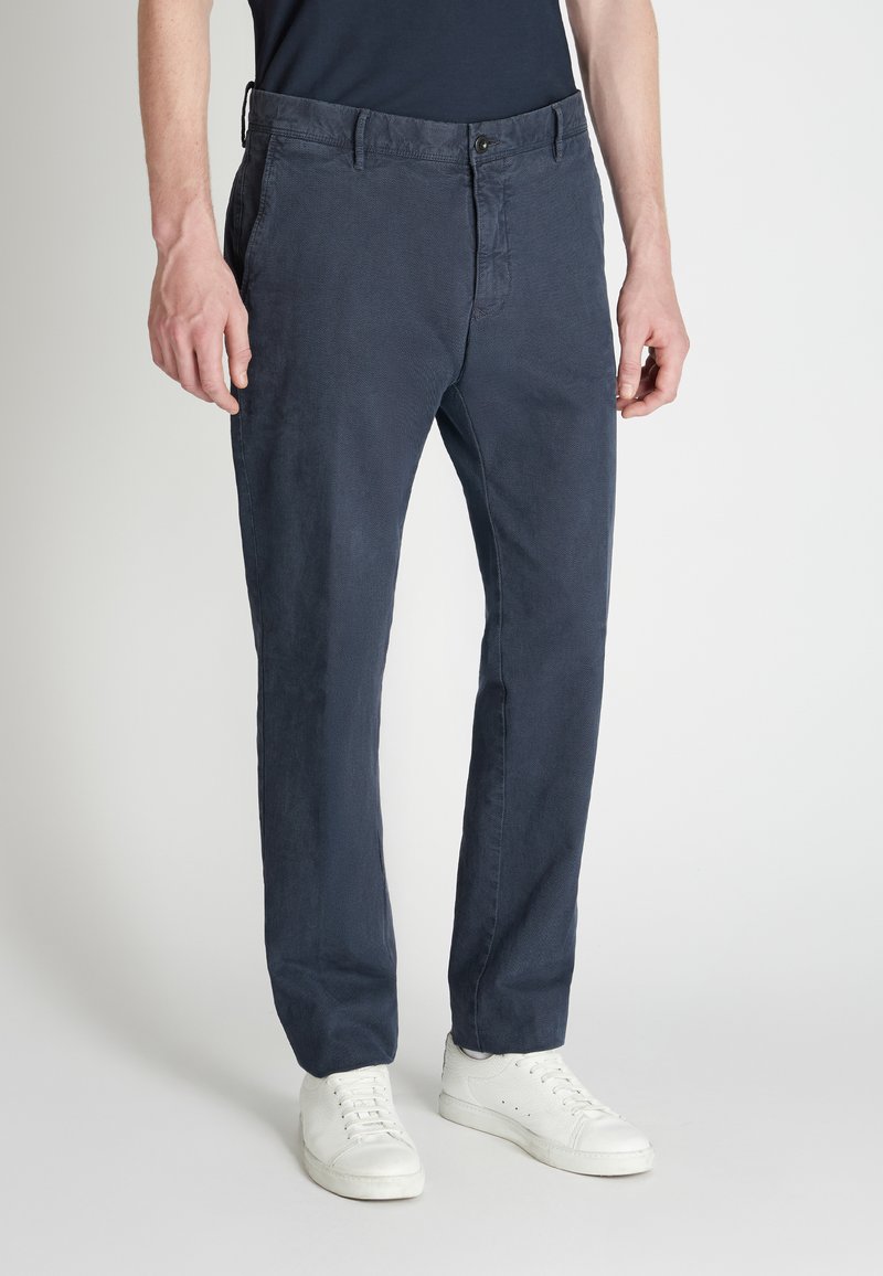 Spodnie chino w granatowym materiale, o prostych nogawkach, z fakturowaną powierzchnią, z przodu zapięcie na guzik, boczne kieszenie, zestawione z białymi trampkami.