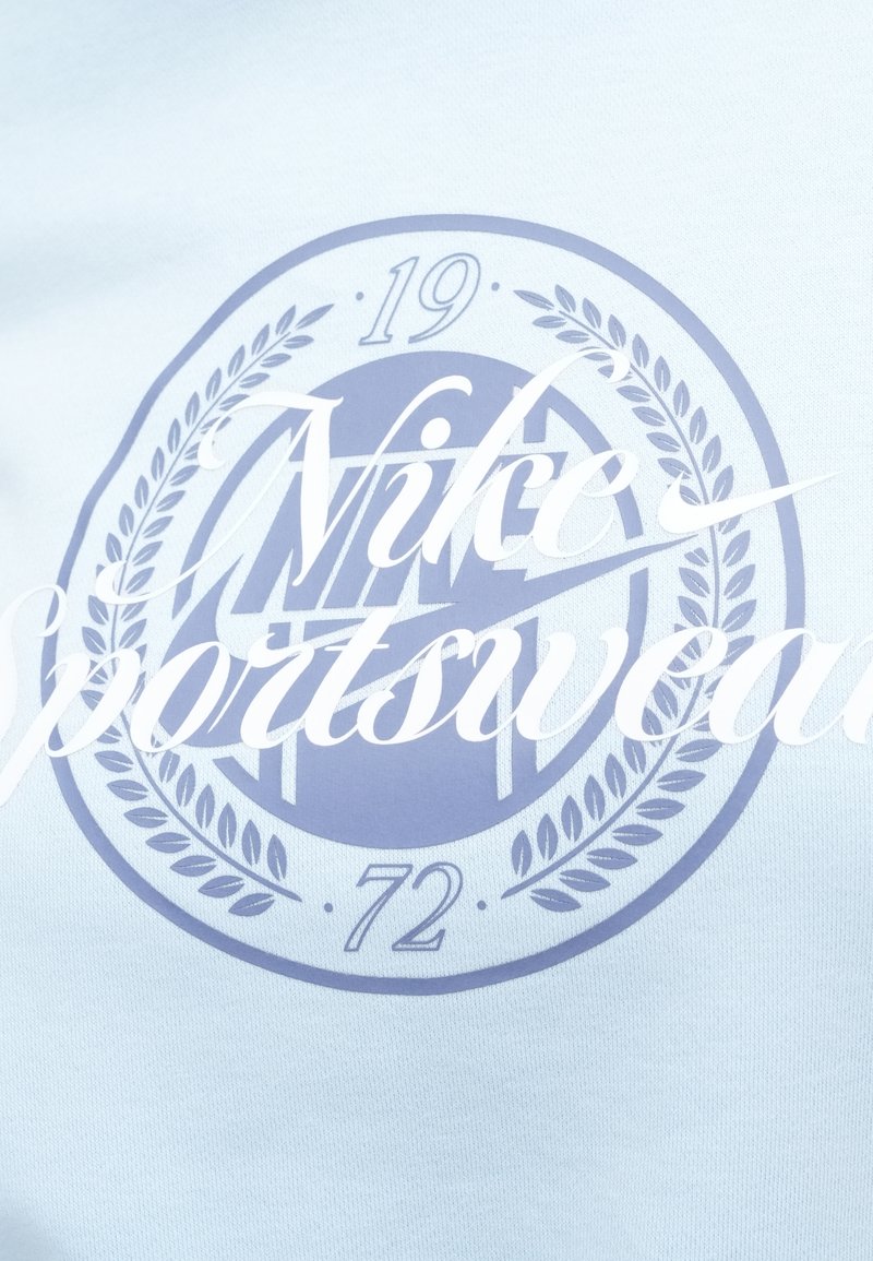 Tissu bleu clair avec un logo circulaire Nike et le texte "Nike Sportswear" en blanc. Comprend les chiffres "19" et "72."