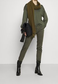 Olivgrön oversized tröja, olivgröna tajta jeans, mörkgrön scarf med fransar, svart vadderad handväska och blanka svarta ankelstövlar.