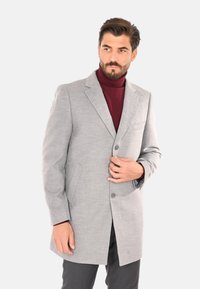 Cappotto grigio in misto lana con rever a punta, chiusura a bottone singolo e doppie tasche frontali, indossato sopra un dolcevita bordeaux.