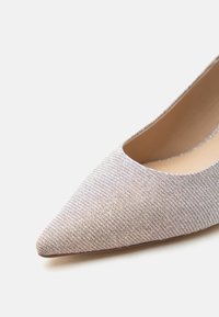 Γυναικείο παπούτσι με μυτερή μύτη, ανώτερο υλικό από ανοιχτό γκρι υφή και μπεζ εσωτερική επένδυση, εμφανίζεται σε λευκό φόντο.