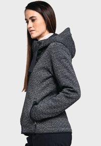 Chaqueta de mezcla de lana gris con un patrón texturizado, capucha, bolsillos con cremallera y un diseño ajustado, que muestra un aspecto moderno y casual.