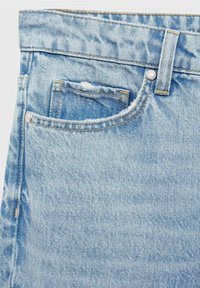 Jeans de denim azul claro con una textura desgastada, costuras distintas y un bolsillo frontal con un ligero desgarro. Detalle de cierre con botón de metal visible.