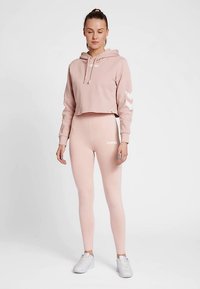 Roze cropped hoodie met een trekkoord en witte letters. Roze legging met een logo, gecombineerd met witte sneakers. Gladde stof en een aansluitend ontwerp.