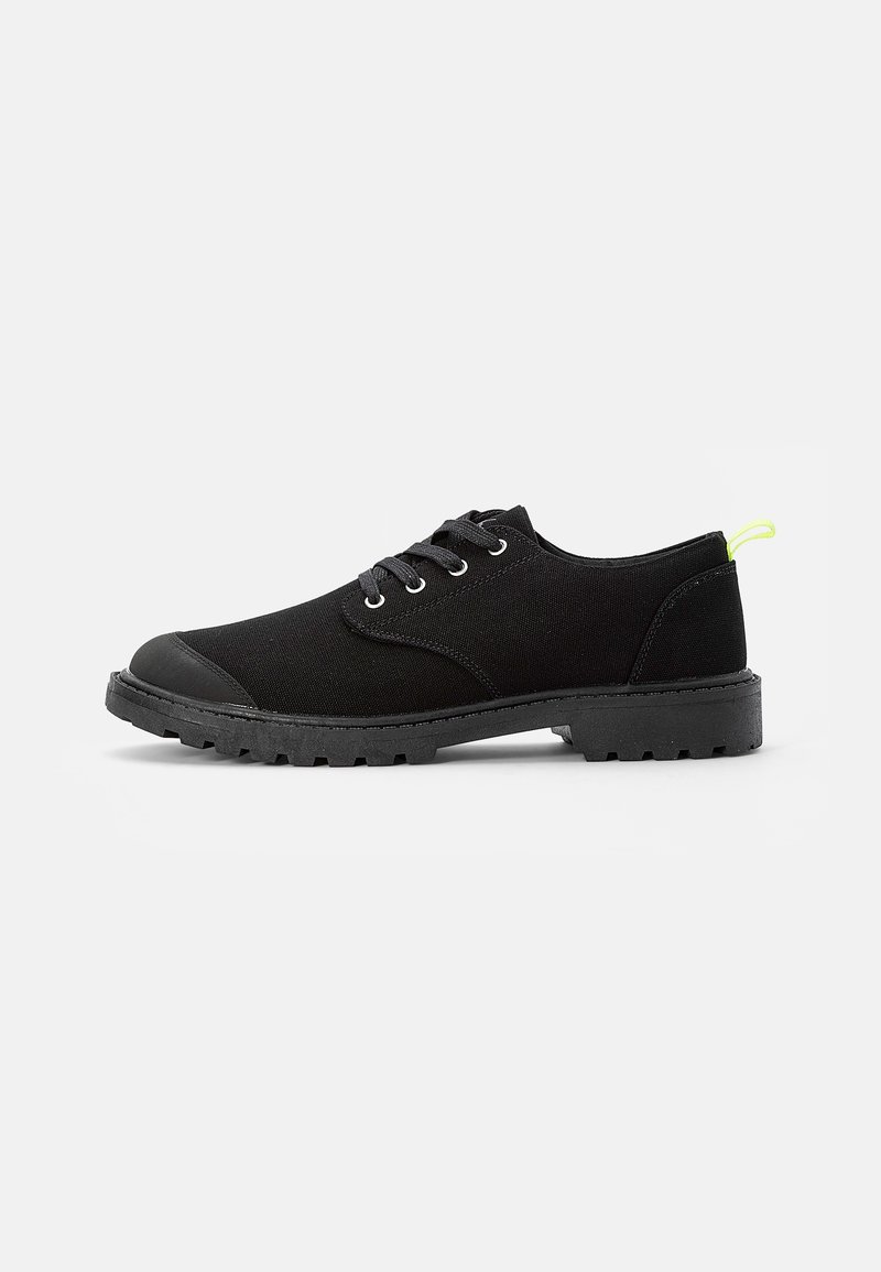 Chaussures noires à lacets avec une tige en toile, un embout en caoutchouc, une semelle texturée et un petit accent vert fluo sur le talon.