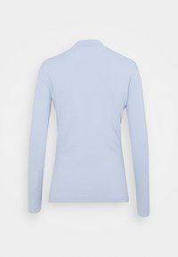 Chemise bleu clair à manches longues avec un col haut, vue de dos sur un fond blanc uni.