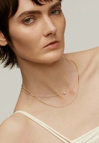 Collares en capas con una cadena de oro y una cadena de plata, adornados con un pequeño acento de diamante, llevados sobre piel desnuda, mostrando simplicidad y elegancia.