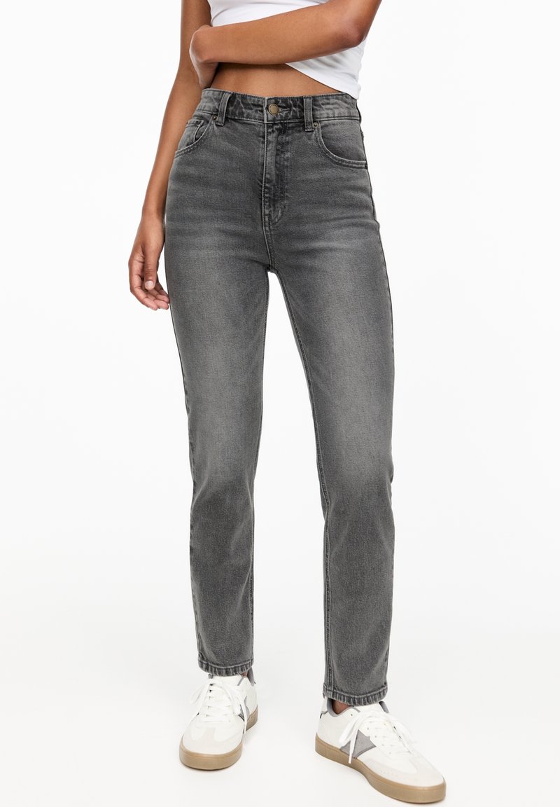 Jean gris taille haute en denim délavé avec une coupe droite, doté de poches avant et d'une fermeture à bouton, assorti à des baskets blanches.