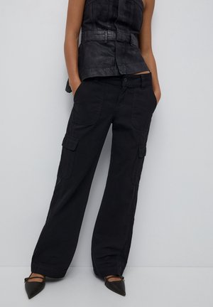 Czarne spodnie bojówkowe o luźnym kroju, z bocznymi kieszeniami i zapięciem na guziki. W zestawie z czarnym topem bez rękawów i czarnymi, spiczastymi butami.