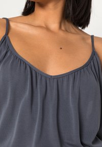 Grijze mouwloze top met een V-halslijn, geplooide details en dunne bandjes. Zachte textuur met een lichte draping.
