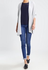 Jasnoszary kardigan z otwartym przodem, połączony z granatowym topem i ciemnoniebieskimi dżinsami. Strój cechuje się luźnym krojem i gładką fakturą.