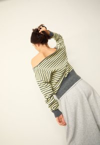 Gestreifter Pullover in Gelb und Grau, schulterfreies Design mit gerippten Bündchen. Kombiniert mit einem grauen, hoch taillierten Rock mit gerafftem Bund.