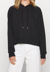 Sudadera negra con un bolsillo frontal, capucha con cordón y puños acanalados. El diseño presenta un corte holgado y está hecha de una tela suave.