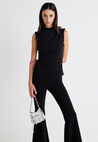 Top negru cu sclipici, cu guler înalt și mâneci scurte, purtat cu pantaloni negri evazați. Ținând o poșetă mică argintie cu accente metalice.