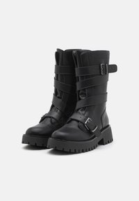 Black faux leather ankle boots with chunky rubber soles, featuring multiple straps and buckle accents for a rugged design.