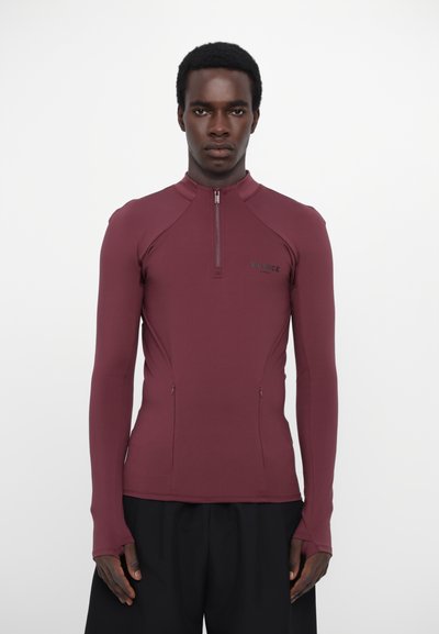 Maroon long-sleeve shirt with half zipper, featuring a fitted design. Smooth texture and zippered side pockets. Logo positioned on chest.