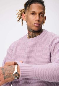Pull lilas avec un côtes texturé, encolure ronde et manches longues. Présente un bracelet en argent au poignet avec un design élaboré.
