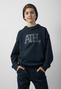 Granatowa bluza z kapturem z du żym szarym logo "ATHL", długie rękawy, kieszeń z przodu oraz regulowany kaptur, zestawiona z pasującymi granatowymi spodniami.