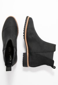 Bottines noires avec une texture lisse imitant le suede, des panneaux latéraux élastiques et une semelle en caoutchouc marron avec un léger talon et une bonne adhérence.