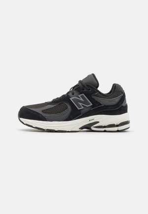 Schwarzer und grauer New Balance 2002R Sneaker mit Obermaterial aus Mesh und Wildleder, weißer gepolsterter Sohle und Schnürsenkeln vor einfarbigem Hintergrund.